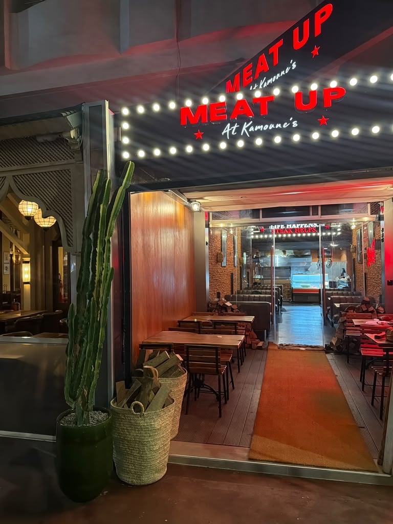 La façade du restaurant le soir : enseigne néon MEAT UP et guirlande d'ampoules